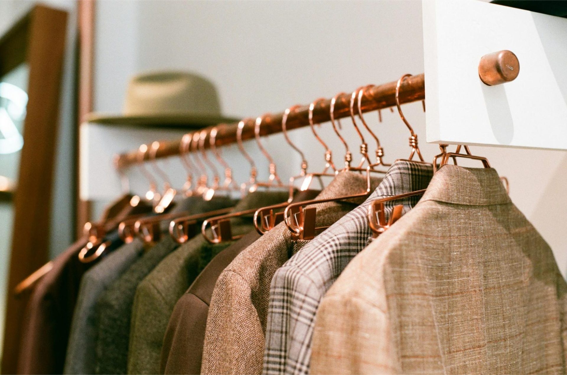 Row of tailored jackets hanging neatly on copper wire hangers.